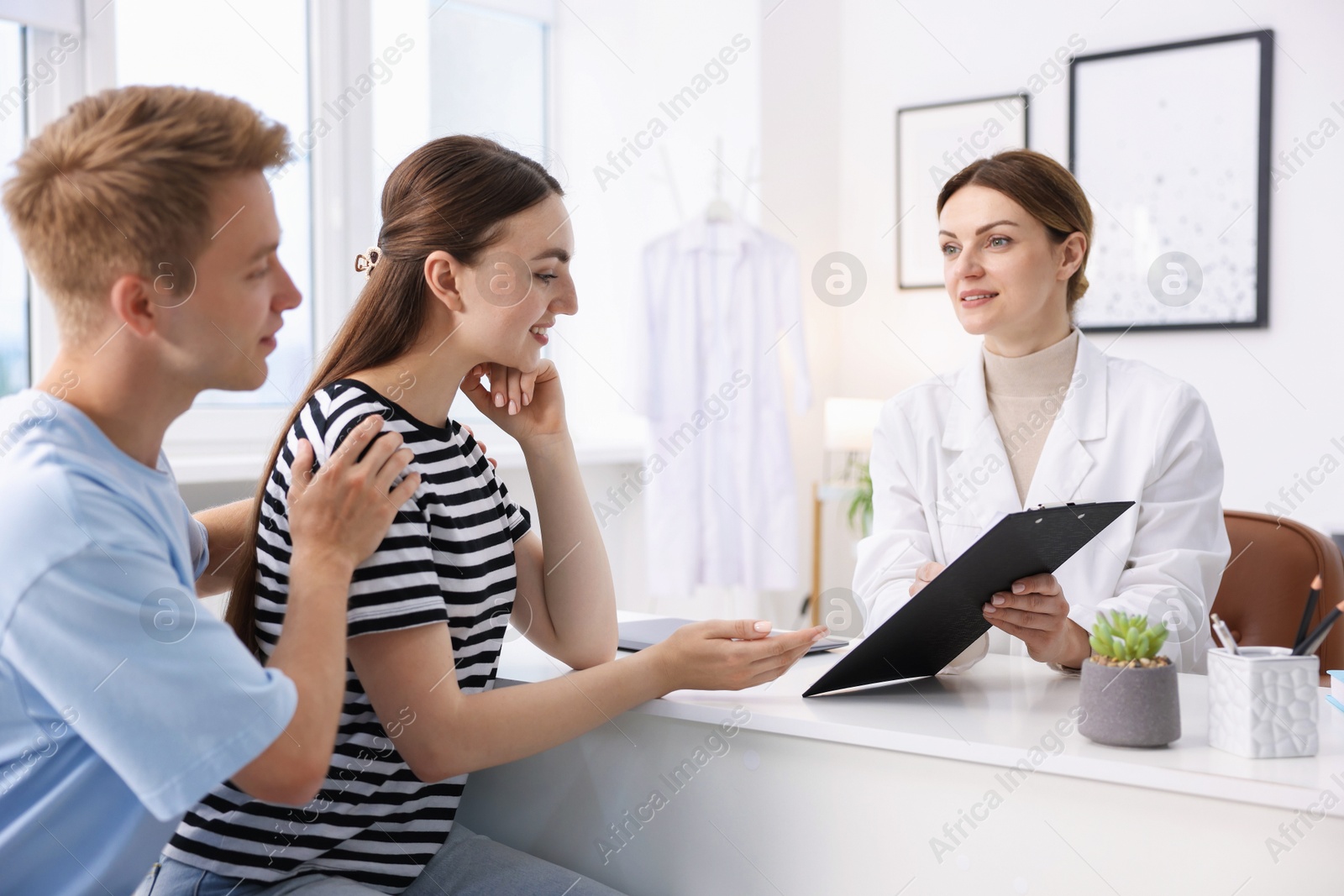 In vitro fertilization (IVF). Doctor showing couple good results on clipboard in reproductive clinic Photo of In vitro fertilization (IVF). Doctor showing couple good results on clipboard in reproductive clinic