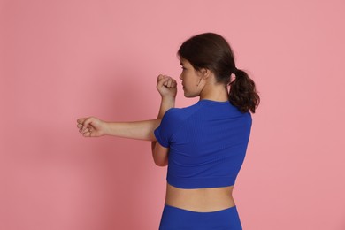 Photo of Teenage girl in sportswear stretching on pink background