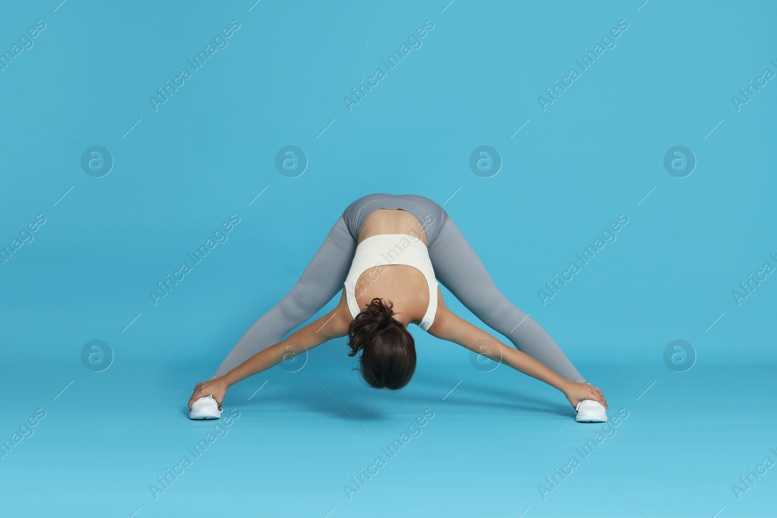 Teenage girl in sportswear stretching on light blue background Photo of Teenage girl in sportswear stretching on light blue background
