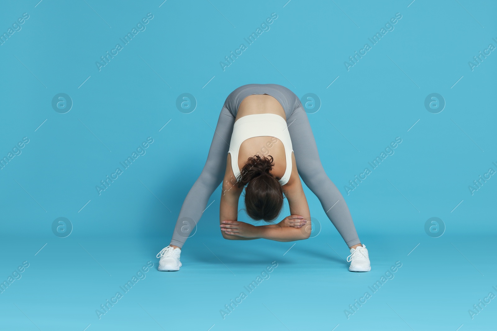 Teenage girl in sportswear stretching on light blue background Photo of Teenage girl in sportswear stretching on light blue background