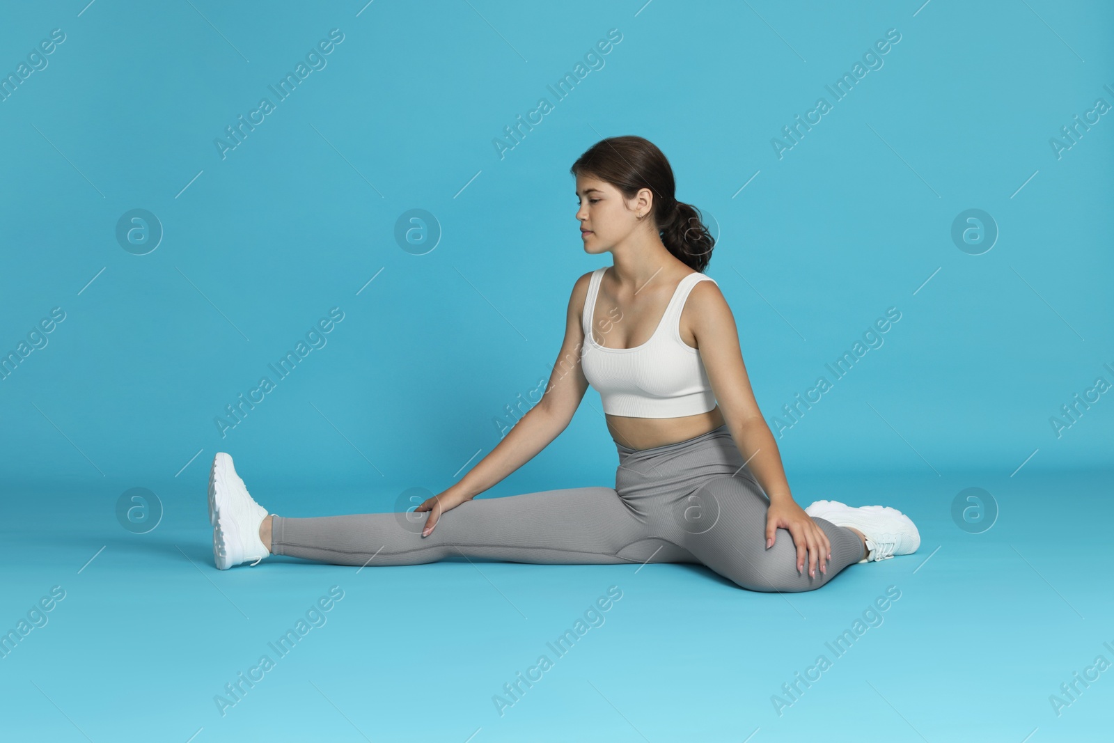 Teenage girl in sportswear stretching on light blue background Photo of Teenage girl in sportswear stretching on light blue background