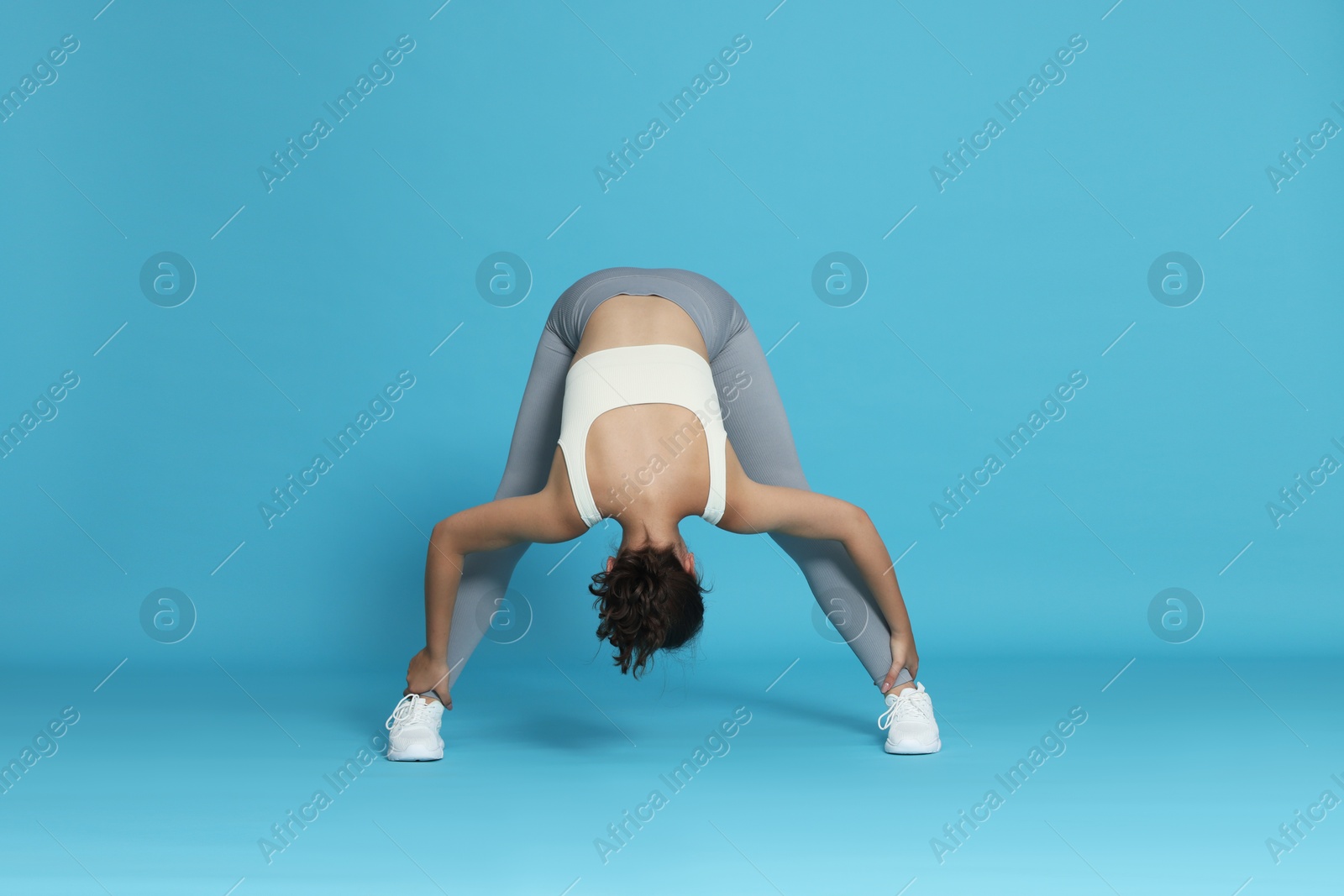 Teenage girl in sportswear stretching on light blue background Photo of Teenage girl in sportswear stretching on light blue background