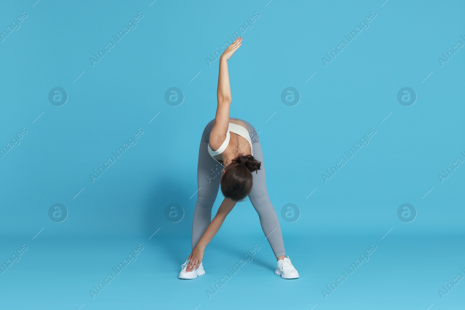 Teenage girl in sportswear stretching on light blue background Photo of Teenage girl in sportswear stretching on light blue background