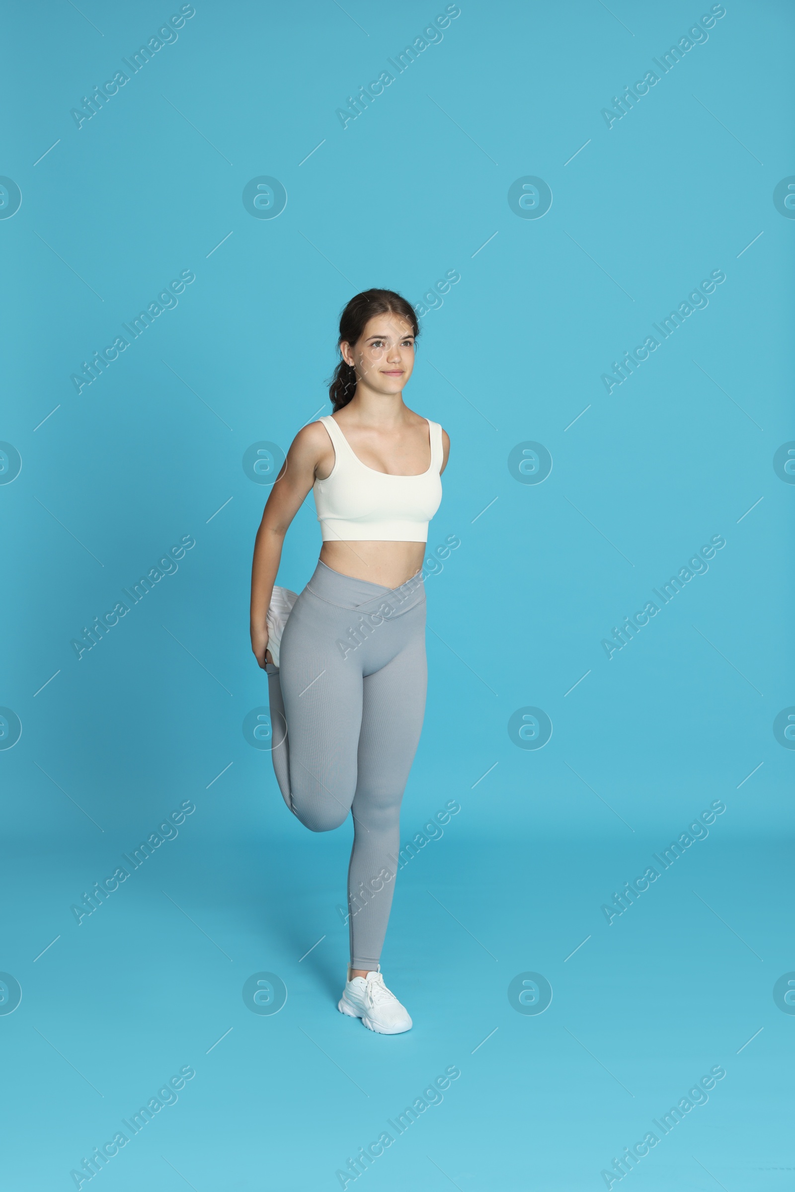 Teenage girl in sportswear stretching on light blue background Photo of Teenage girl in sportswear stretching on light blue background