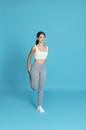 Photo of Teenage girl in sportswear stretching on light blue background