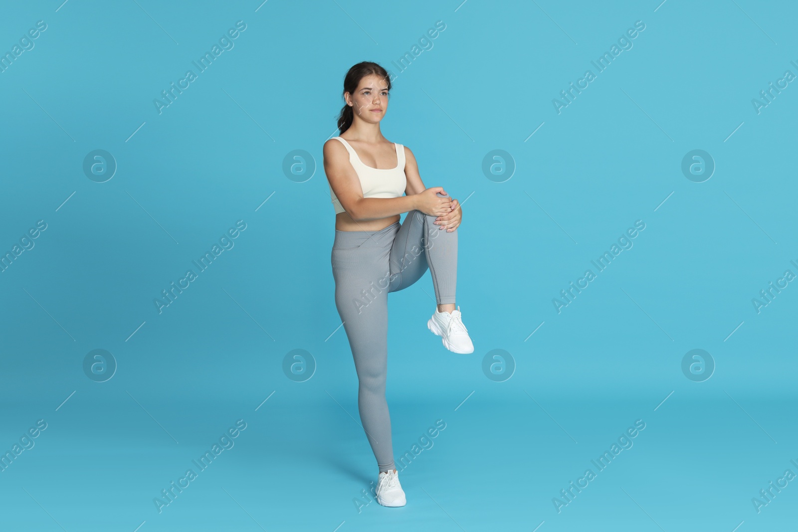 Teenage girl in sportswear stretching on light blue background Photo of Teenage girl in sportswear stretching on light blue background