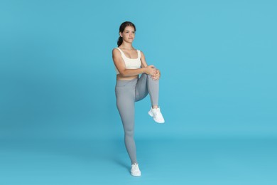 Photo of Teenage girl in sportswear stretching on light blue background