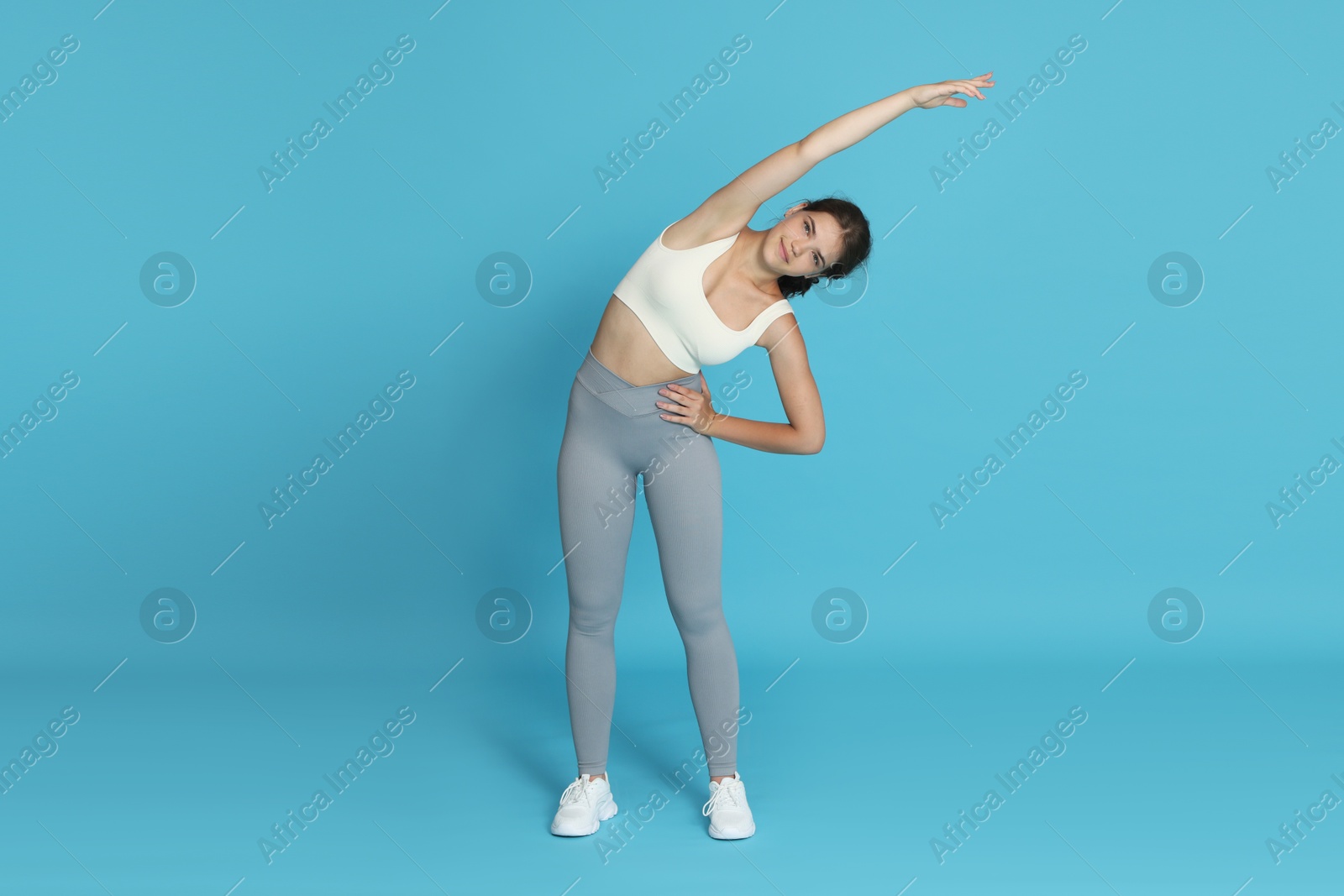 Teenage girl in sportswear stretching on light blue background Photo of Teenage girl in sportswear stretching on light blue background