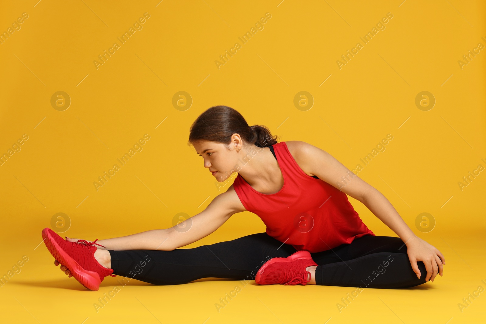 Teenage girl in sportswear stretching on orange background Photo of Teenage girl in sportswear stretching on orange background