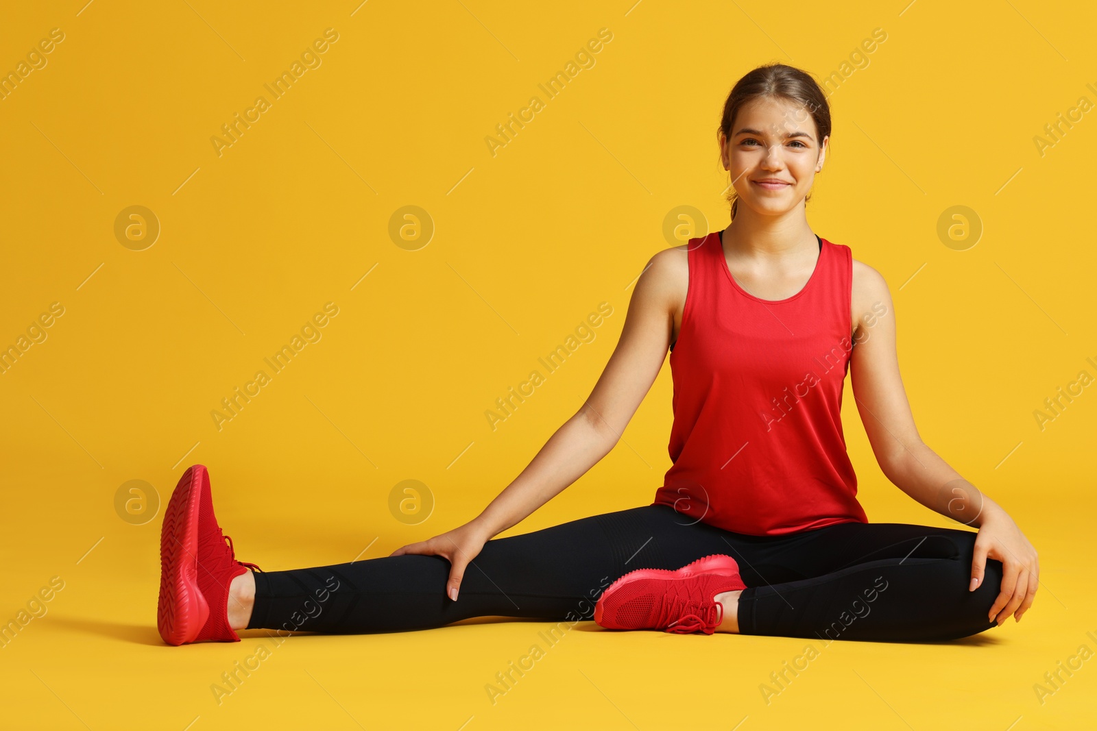 Teenage girl in sportswear stretching on orange background Photo of Teenage girl in sportswear stretching on orange background