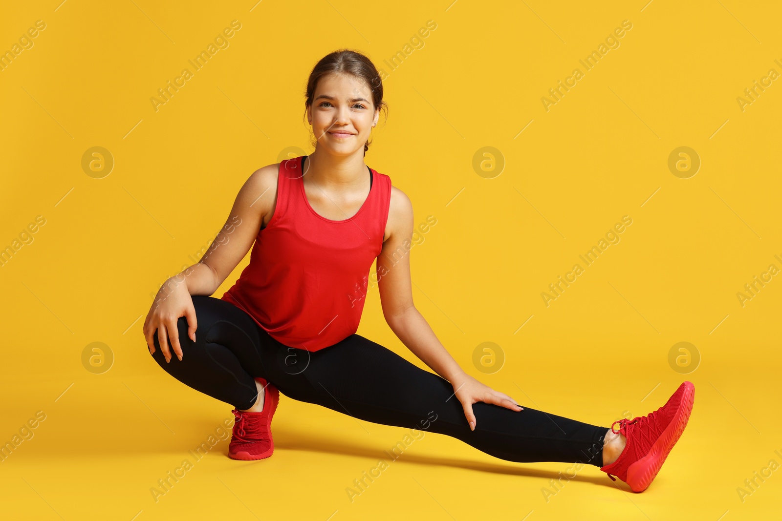 Teenage girl in sportswear stretching on orange background Photo of Teenage girl in sportswear stretching on orange background