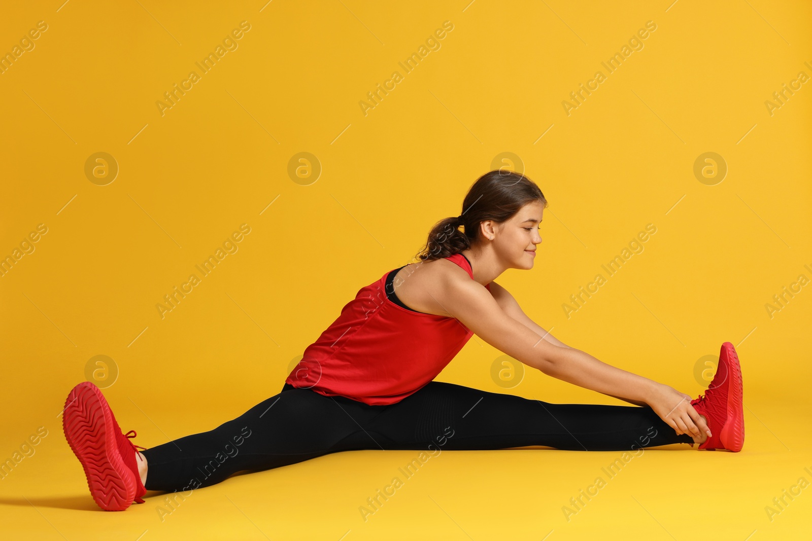 Teenage girl in sportswear stretching on orange background Photo of Teenage girl in sportswear stretching on orange background