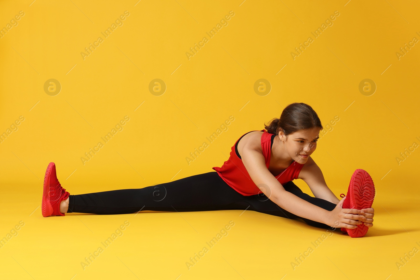 Teenage girl in sportswear stretching on orange background Photo of Teenage girl in sportswear stretching on orange background