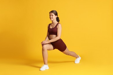 Photo of Teenage girl in sportswear stretching on orange background