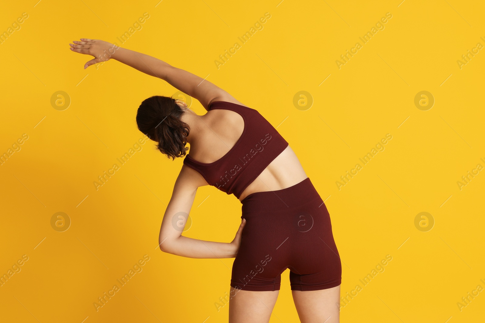 Teenage girl in sportswear stretching on orange background, back view Photo of Teenage girl in sportswear stretching on orange background, back view