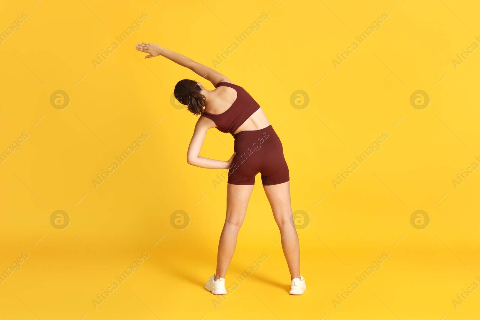 Teenage girl in sportswear stretching on orange background, back view Photo of Teenage girl in sportswear stretching on orange background, back view
