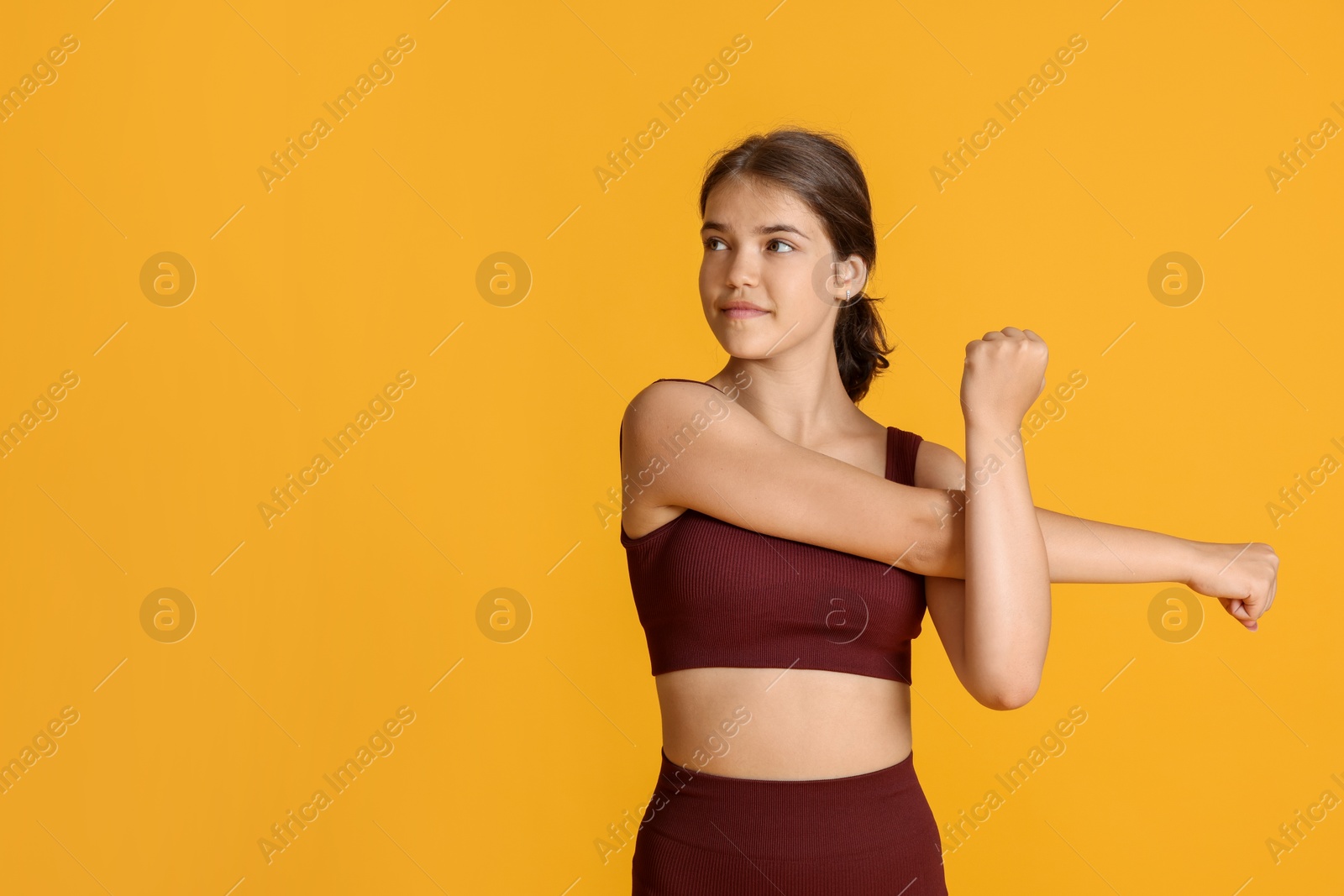 Teenage girl in sportswear stretching on orange background, space for text Photo of Teenage girl in sportswear stretching on orange background, space for text