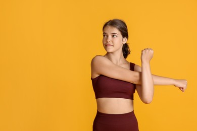 Photo of Teenage girl in sportswear stretching on orange background, space for text