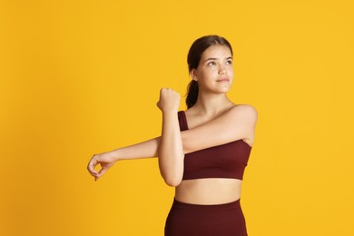 Photo of Teenage girl in sportswear stretching on orange background