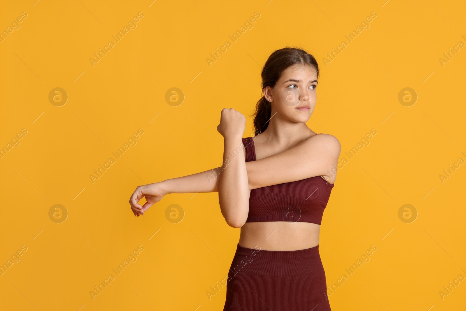 Teenage girl in sportswear stretching on orange background, space for text Photo of Teenage girl in sportswear stretching on orange background, space for text