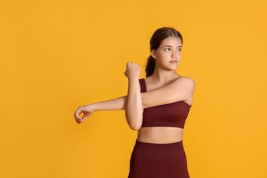 Photo of Teenage girl in sportswear stretching on orange background, space for text