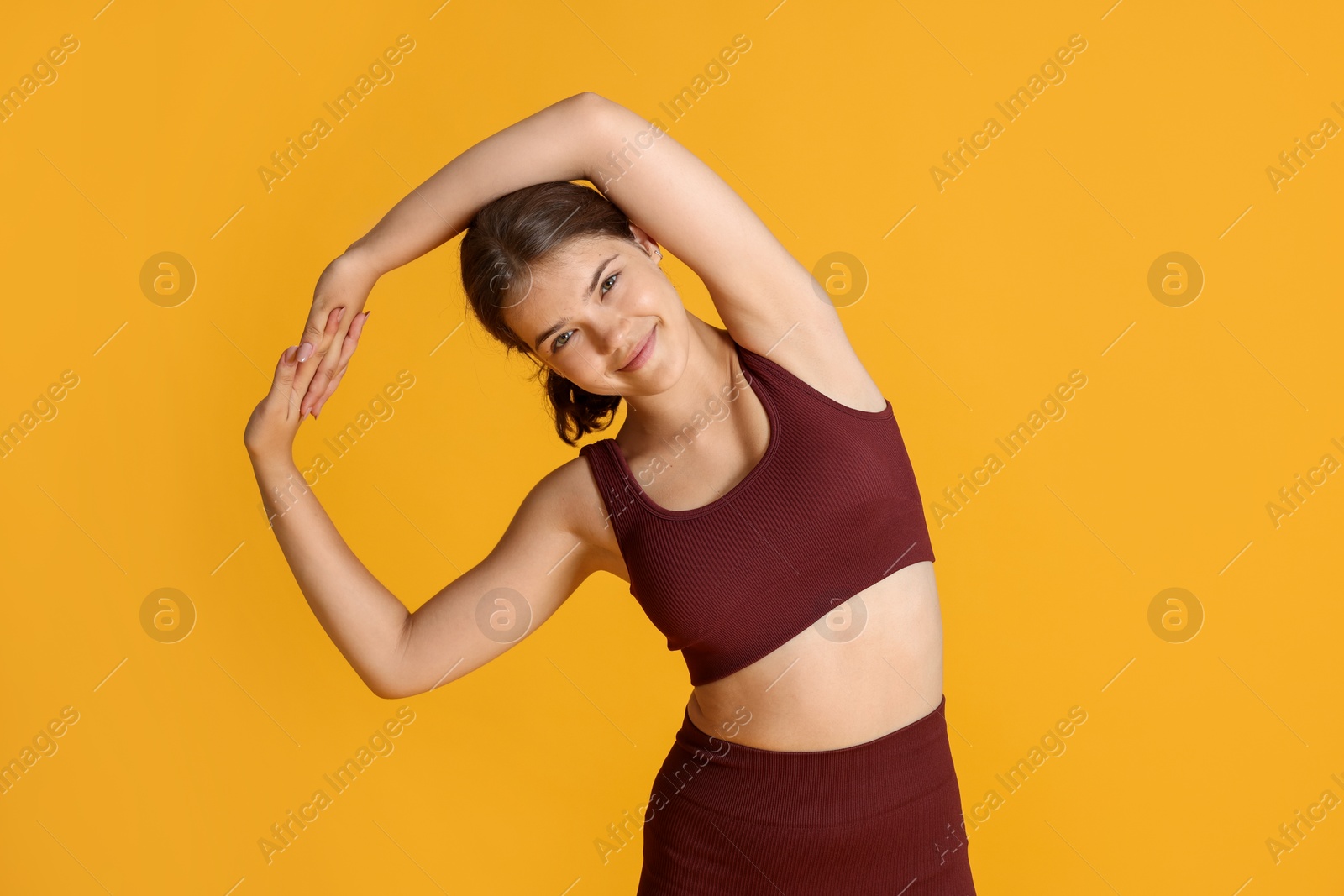 Teenage girl in sportswear stretching on orange background Photo of Teenage girl in sportswear stretching on orange background