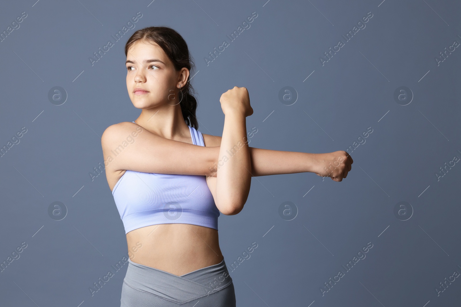 Teenage girl in sportswear stretching on grey background Photo of Teenage girl in sportswear stretching on grey background