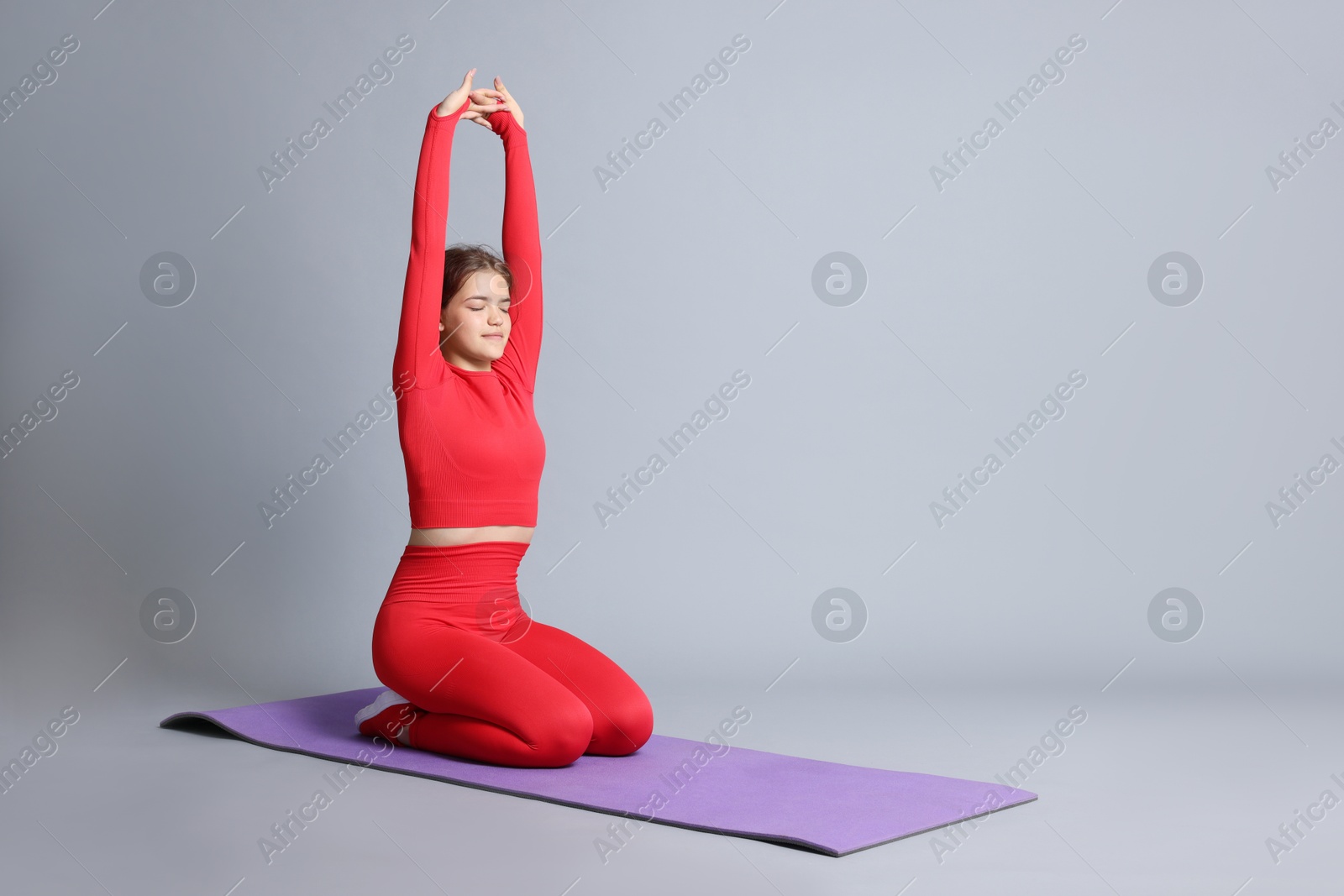 Teenage girl in sportswear stretching on mat against grey background, space for text Photo of Teenage girl in sportswear stretching on mat against grey background, space for text