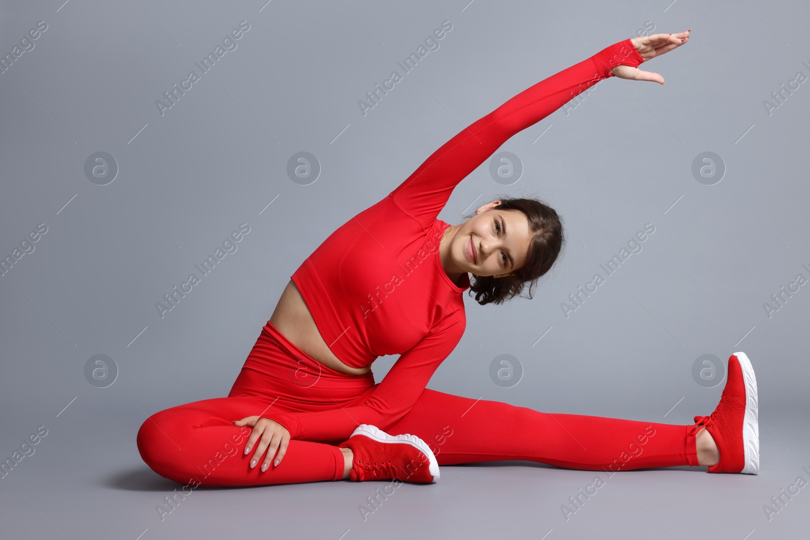 Teenage girl in sportswear stretching on grey background Photo of Teenage girl in sportswear stretching on grey background
