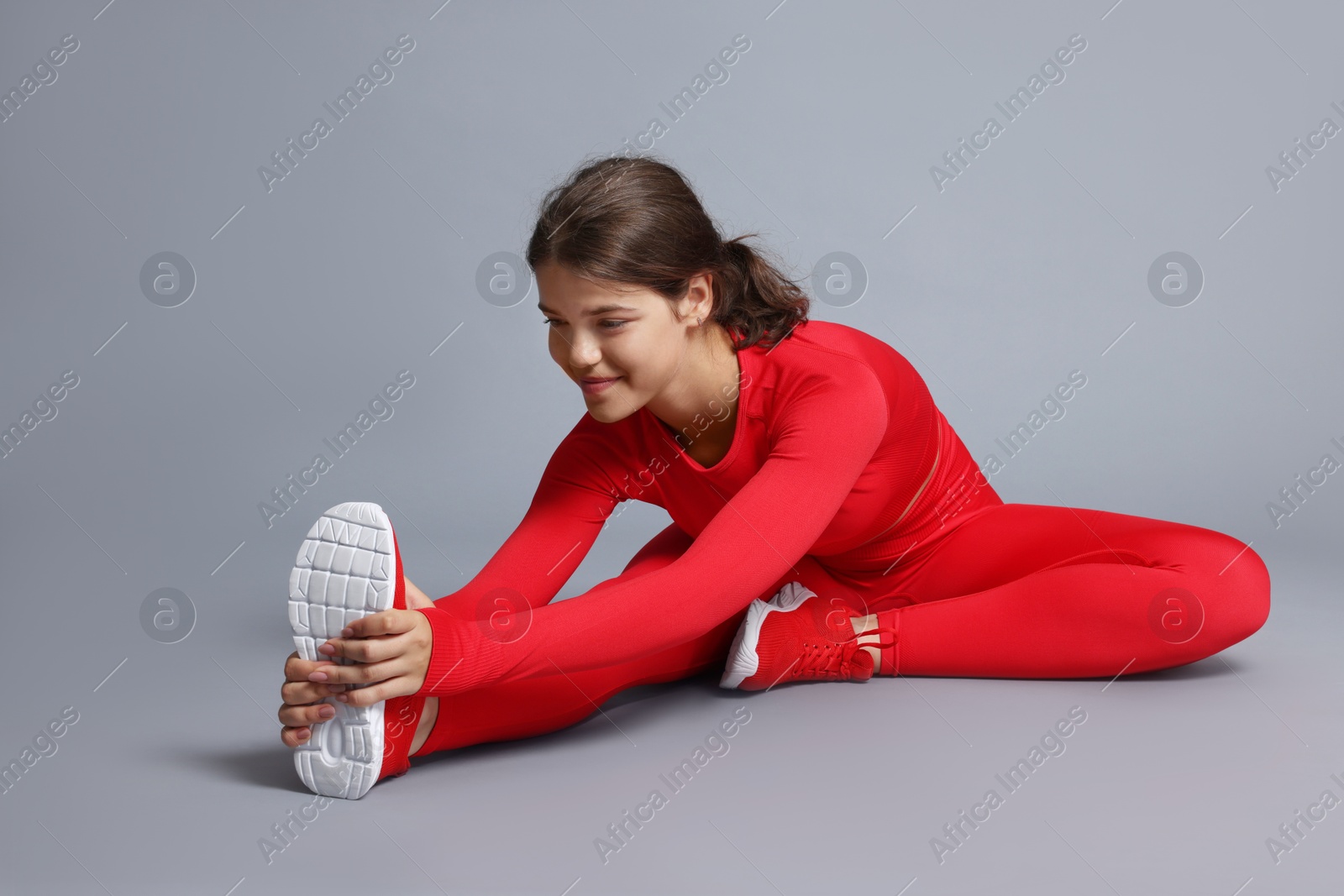 Teenage girl in sportswear stretching on grey background Photo of Teenage girl in sportswear stretching on grey background
