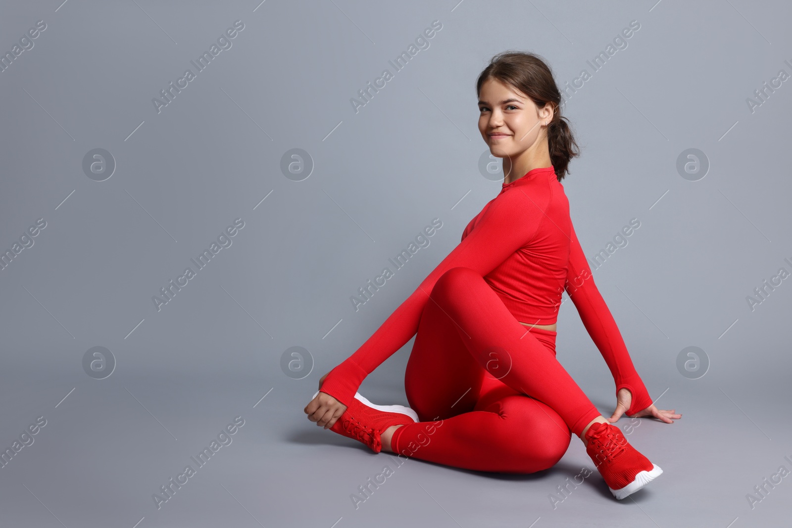 Teenage girl in sportswear stretching on grey background, space for text Photo of Teenage girl in sportswear stretching on grey background, space for text