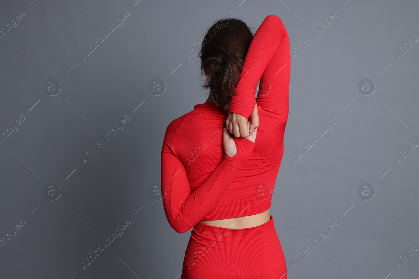 Teenage girl in sportswear stretching on grey background, back view. Space for text Photo of Teenage girl in sportswear stretching on grey background, back view. Space for text
