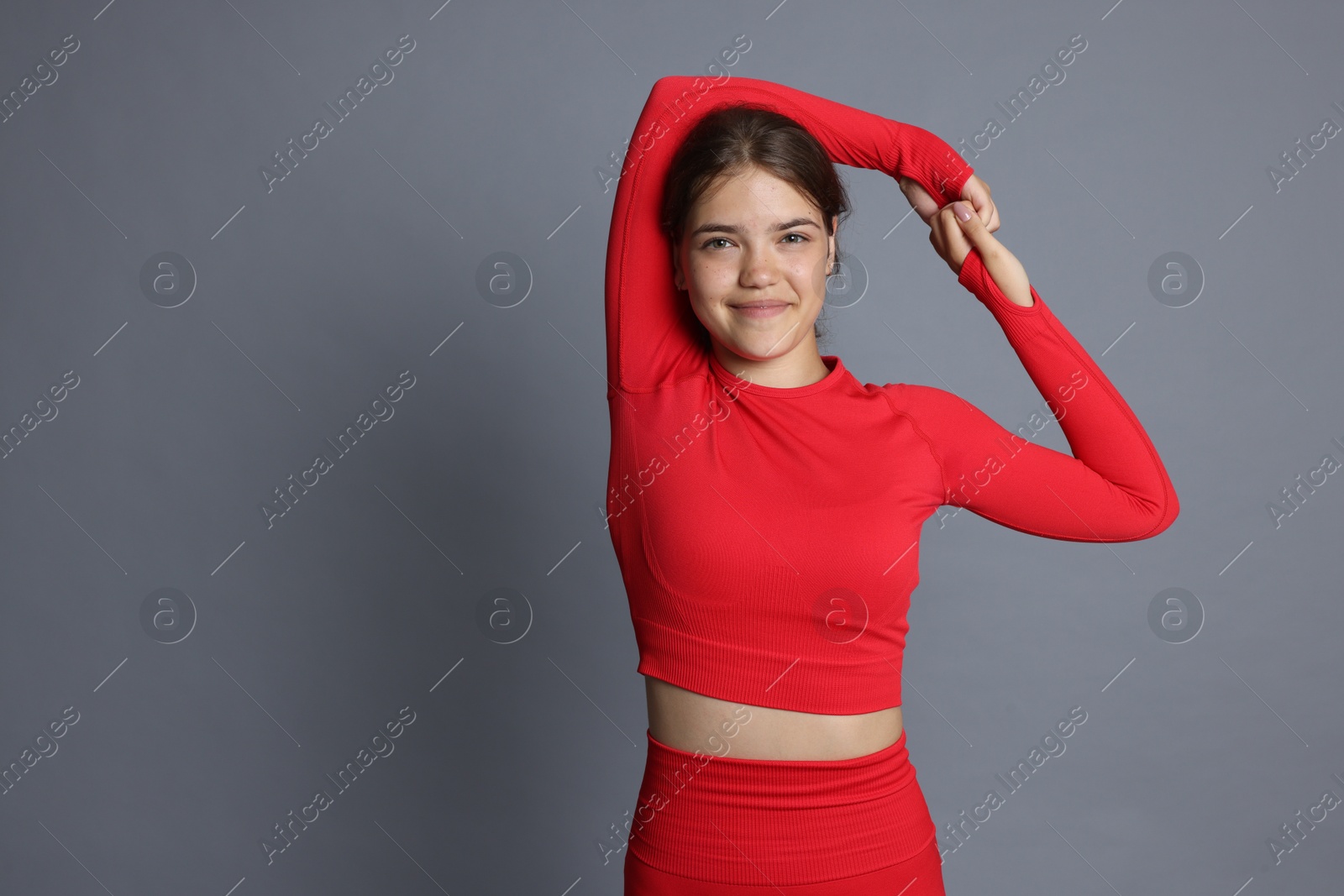 Teenage girl in sportswear stretching on grey background, space for text Photo of Teenage girl in sportswear stretching on grey background, space for text