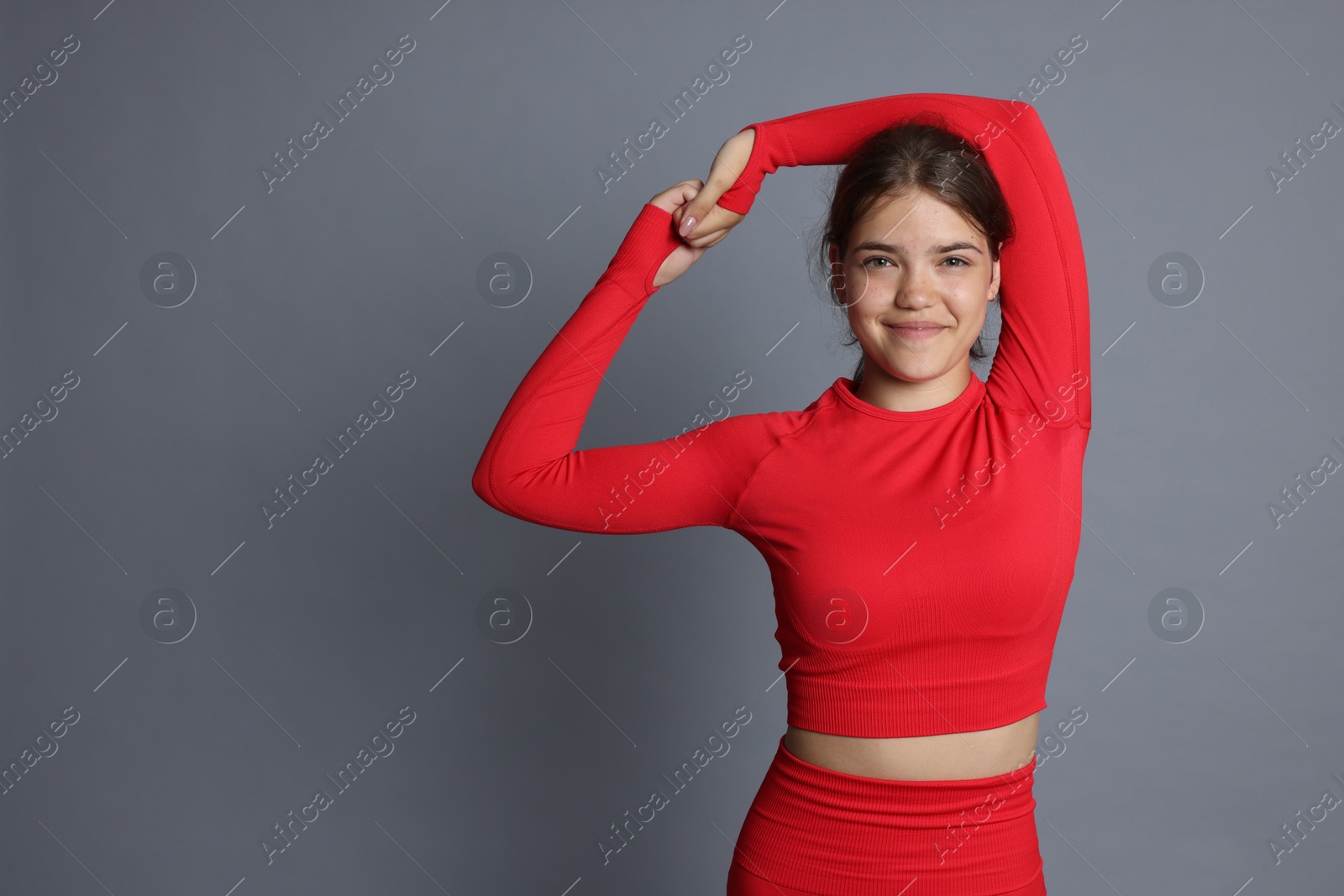 Teenage girl in sportswear stretching on grey background, space for text Photo of Teenage girl in sportswear stretching on grey background, space for text