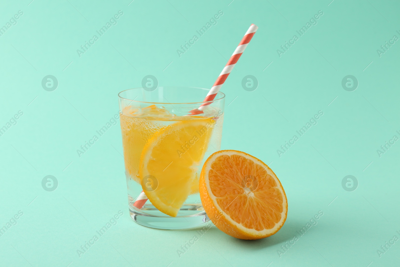 Photo of Sparkling water with orange slices in glass and fresh fruit on turquoise background