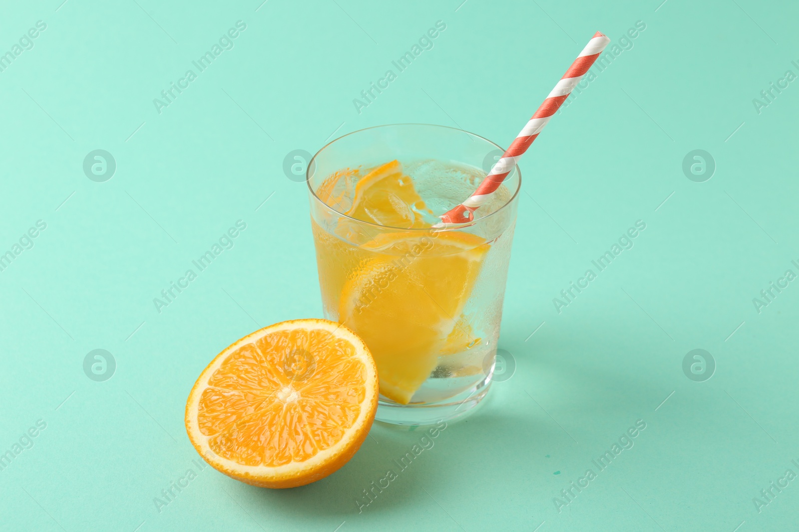 Photo of Sparkling water with orange slices in glass and fresh fruit on turquoise background, closeup