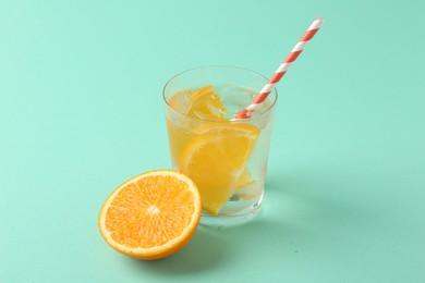 Photo of Sparkling water with orange slices in glass and fresh fruit on turquoise background, closeup