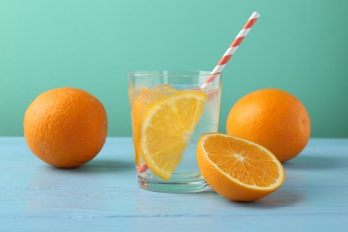 Photo of Sparkling water with orange slices in glass, fresh fruits and straws on light blue wooden table against turquoise background