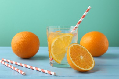 Photo of Sparkling water with orange slices in glass, fresh fruits and straws on light blue wooden table against turquoise background, closeup