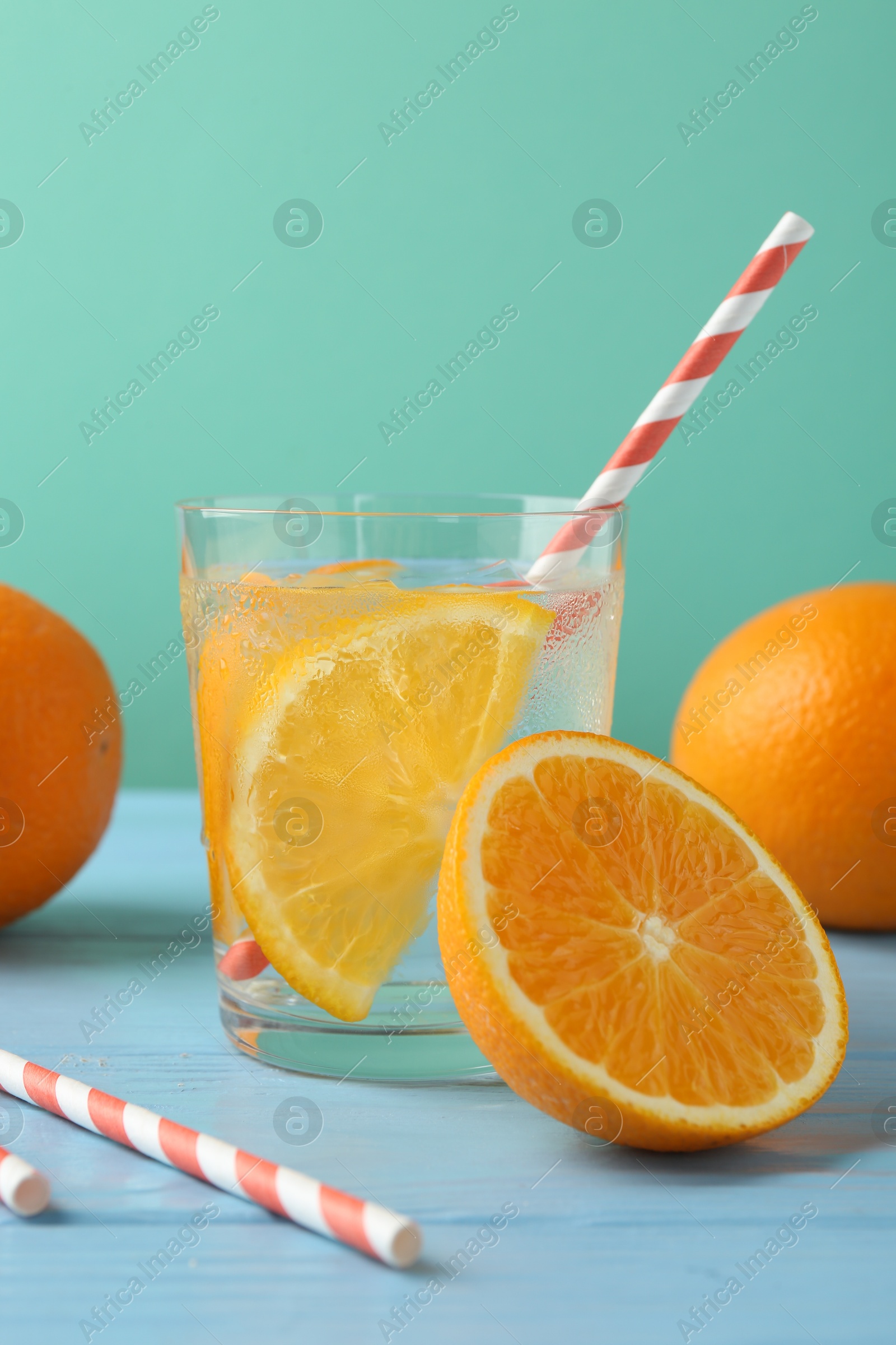 Photo of Sparkling water with orange slices in glass, fresh fruits and straws on light blue wooden table against turquoise background, closeup