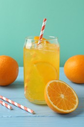 Photo of Sparkling water with orange slices in glass, fresh fruits and straws on light blue wooden table against turquoise background, closeup