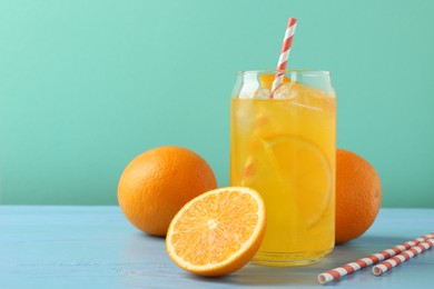 Photo of Sparkling water with orange slices in glass, fresh fruits and straws on light blue wooden table against turquoise background, closeup. Space for text