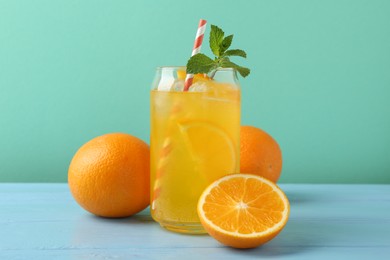Photo of Sparkling water with orange slices in glass, fresh fruits and mint on light blue wooden table against turquoise background
