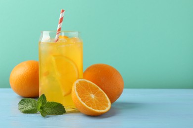 Photo of Sparkling water with orange slices in glass, fresh fruits and mint on light blue wooden table against turquoise background, space for text