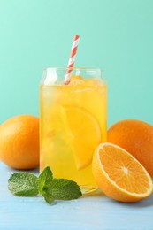 Photo of Sparkling water with orange slices in glass, fresh fruits and mint on light blue wooden table against turquoise background, closeup