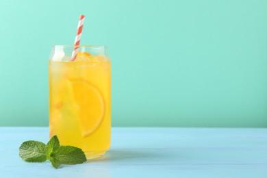 Photo of Refreshing soda water with orange slices in glass and mint on light blue wooden table against turquoise background, space for text