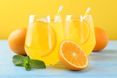 Photo of Refreshing soda water with orange slices in glasses, mint and fresh fruits on light blue wooden table, closeup