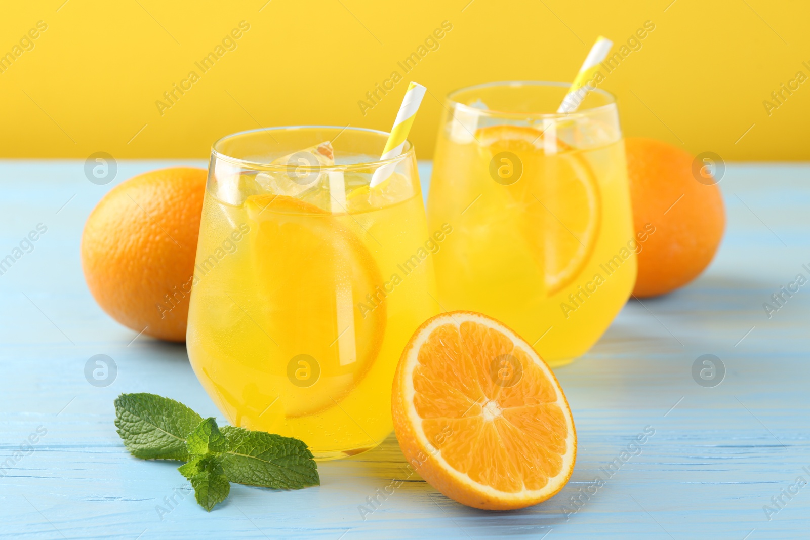 Photo of Refreshing soda water with orange slices in glasses, mint and fresh fruits on light blue wooden table, closeup
