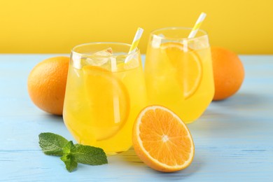 Photo of Refreshing soda water with orange slices in glasses, mint and fresh fruits on light blue wooden table, closeup