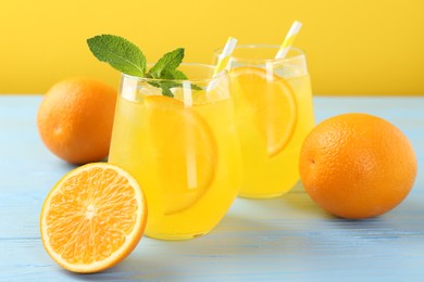Photo of Refreshing soda water with orange slices in glasses, mint and fresh fruits on light blue wooden table, closeup